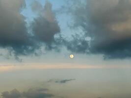 A serene twilight sky displays the moon amidst scattered clouds, creating a peaceful and contemplative atmosphere. The gentle hues of blue and gray enhance the tranquil evening scene. photo