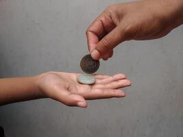 Close-up of a hand placing a coin into another open palm, symbolizing generosity and financial exchange. The image captures a moment of sharing and monetary transaction. photo