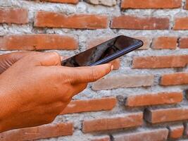 Close-up of a hand holding a smartphone against a brick wall background, symbolizing connectivity and modern technology. The image captures a moment of digital interaction and communication. photo