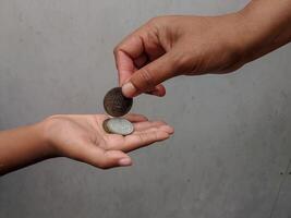 Two hands engaged in a coin exchange, highlighting themes of charity, giving, and economic interaction. The simple backdrop emphasizes the focus on human connection and finance. photo