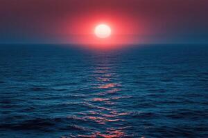Big red sun setting on calm ocean creating pink reflections photo
