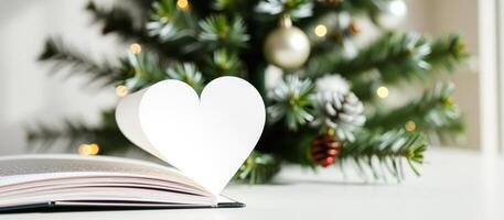 Open book with heart shape on white background near a Christmas tree photo