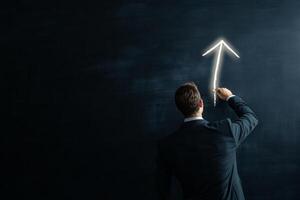 A businessman in his 30s draws a glowing upward arrow on a blackboard in a dimly lit room, symbolizing leadership photo