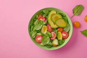 Fresh mixed greens salad bowl with cherry tomatoes and avocado on a pink background photo
