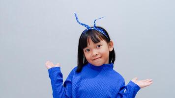 Beautiful smiling happy little asian girl in blue outfit. Charming female child open hands palm up holding something on isolated grey background. Adorable pretty child and copy space. photo