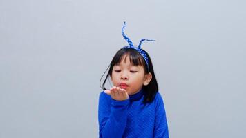 Little Asian girl wearing blue outfit blows with an empty hand, isolated on grey photo