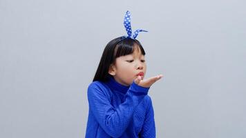 Little Asian girl wearing blue outfit blows with an empty hand, isolated on grey photo