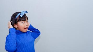 Beautiful Asian child holding hand near ear trying to listen to interesting news expressing communication concept and gossip over grey background photo