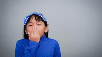 Sleepy child girl yawning while covering her mouth isolated on grey background photo
