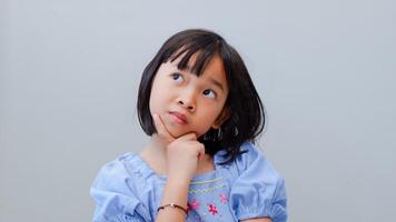portrait of asian beautiful little girl holding chin, thinking concept with light color background. photo
