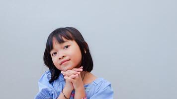Happy adorable cute Asian girl folding hands together, asking buy new toy, sweets or need help. Smiling hopeful black-haired kid child, isolated on grey studio background. May I please concept. photo
