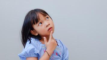 portrait of asian beautiful little girl holding chin, thinking concept with light color background. photo