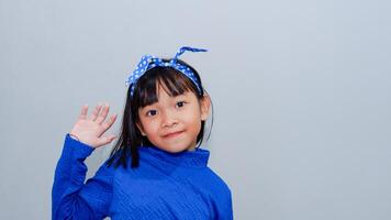 cheerful girl playing wearing blue outfit showing hand of waving hi hello greetings, isolated on light grey background. photo