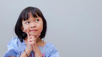 portrait of asian beautiful little girl holding chin, thinking concept with light color background. photo