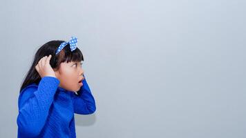 Beautiful Asian child holding hand near ear trying to listen to interesting news expressing communication concept and gossip over grey background photo