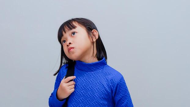 Student girl with backpack standing and thinking an idea on grey background photo