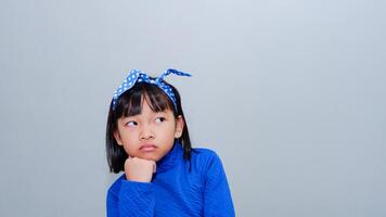 Serious pensive Asian cute kid girl looking away lost in thoughts having question, thoughtful face holding hand under chin dreaming, feeling curious, melancholic or bored. photo
