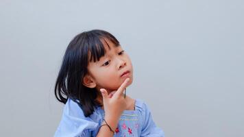 portrait of asian beautiful little girl holding chin, thinking concept with light color background. photo