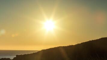 The sun is setting over the ocean and a person is standing on a hill video