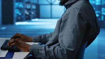 African american man working in server hub capable of processing vast amounts of data. IT programmer at PC desk typing on keyboard, updating servers controlling network resources, close up shot video