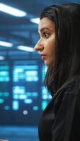 Vertical Meticulous engineer inspecting operational server rows in computer network security data center. Woman supervising supercomputers providing processing and memory resources for various workloads video