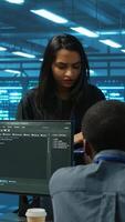 Vertical Manager overseeing server room, walking around with checklist on laptop, troubleshooting hardware and discussing with employees. Supervisor doing inspection in server hub, taking feedback from workers video