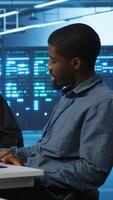 Vertical Multiracial team of IT engineers in server room brainstorming ways to fix equipment storing datasets. Indian and african american coworkers discussing how to mend racks doing computational operations video