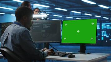Programmer coding on isolated screen computer in data center, supervising server rows in computer network security data center. IT technician overseeing supercomputers using chroma key PC monitor video