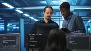 Multiethnic coworkers in server room collaborating to fix servers providing computing resources for workloads. Diverse team of admins supervising data center supercomputers video