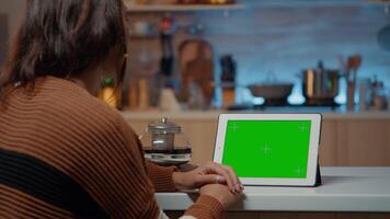 Festive woman looking at green screen display on tablet in decorated kitchen. Young person using digital modern technology device for chroma key background and infographics mock up video