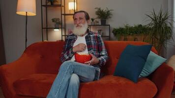 Man sitting on couch eating popcorn and watching interesting TV serial, sport game online at home video