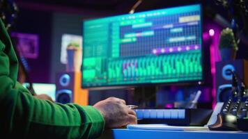 In his home studio, songwriter writes down lines and melodic elements to create new tunes. Using digital audio workstation software, composing and recording songs in post production. Camera B. video