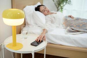 Sleeping asian woman turning off alarm on smartphone while being Waken up in the morning photo