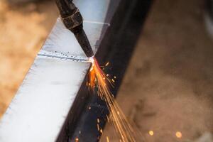 Skilled welder cuts metal with a gas torch in industrial workshop. Sparks fly during precision fabrication process. Craftsman control and expertise in metalworking. Gas torch cuts through steel. photo