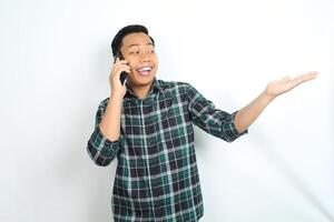 cheerful and carefree asian man wearing casual clothes presenting empty hand while talking on cellphone, calling, with smiling face isolated on white background photo