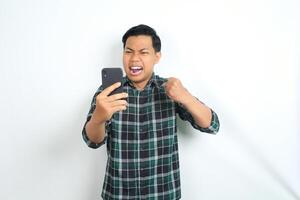 furious asian man shouting while holding cellphone and raising his hand show angry face isolated on white background photo