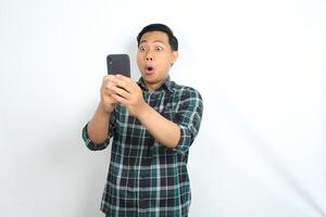 surprised asian man looking at smartphone with shocked face, wow expression, isolated on white background photo