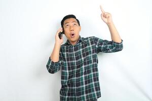 asian man pointing hand with shocked expression while talking on smartphone isolated on white background photo