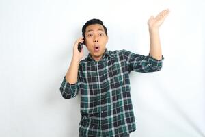 asian man presenting hand with shocked expression while talking on smartphone isolated on white background photo