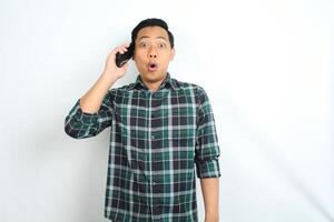 asian man shocked while talking on cellphone isolated on white background photo
