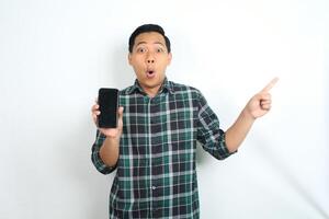 attractive asian man show smartphone screen with pointing hand and surprised face expression isolated on white background photo