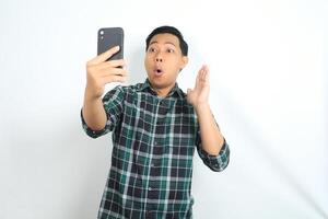 surprised asian man looking at smartphone with shocked face, wow expression, and raising hands, isolated on white background photo