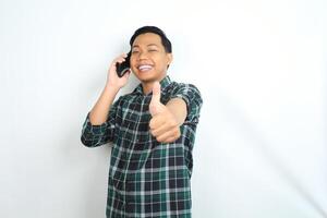 happy and playful asian man give thumbs up while talking on smartphone with smiling face isolated on white background photo
