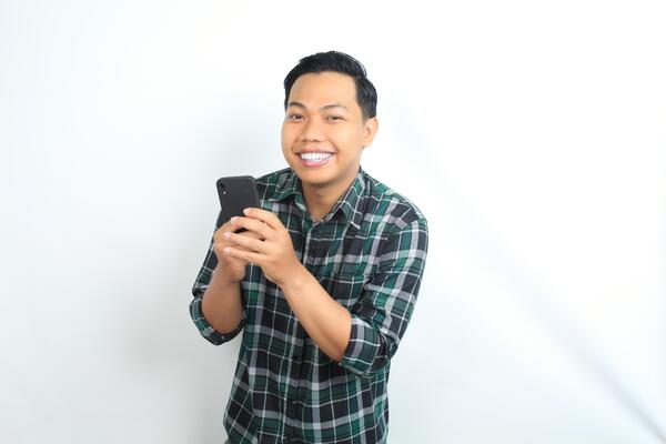 happy asian man wearing casual shirt holding cellphone read news, message, and chatting with smiling face isolated on white background