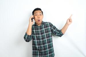 asian man pointing hand with shocked expression while talking on smartphone isolated on white background photo