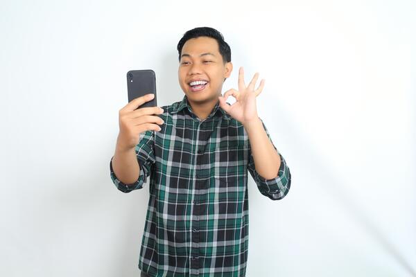 happy asian man holding smartphone wear casual shirt show ok sign, approved, yes gesture, with smiling face isolated on white background