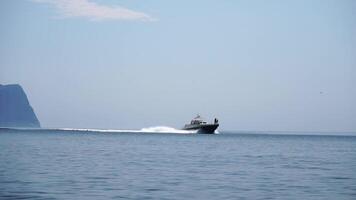 Boat Water Coastline - A small boat sails across calm water towards a distant mountain in the background. video