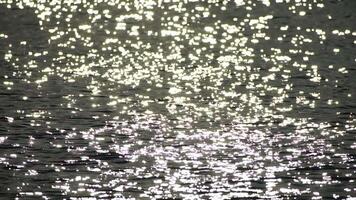 Abstract shining sun reflections on blue surface of sea waves. Bokeh sun glare reflected in water surface. The shimmering small sea waves in sun. Sea on sunny day. Natural bokeh texture. Slow motion video
