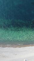 Aerial vertical view of beach with wave caressing shore. Sun glare, small waves on the water surface. Sunset. Evening. Nobody. No people. Summer travel and vacation. video