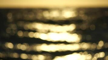 Blurred golden sea at sunset. The sun reflects and sparkles on the waves with bokeh, illuminating the golden sea. Holiday recreation concept. Abstract nautical summer ocean sunset nature background. video